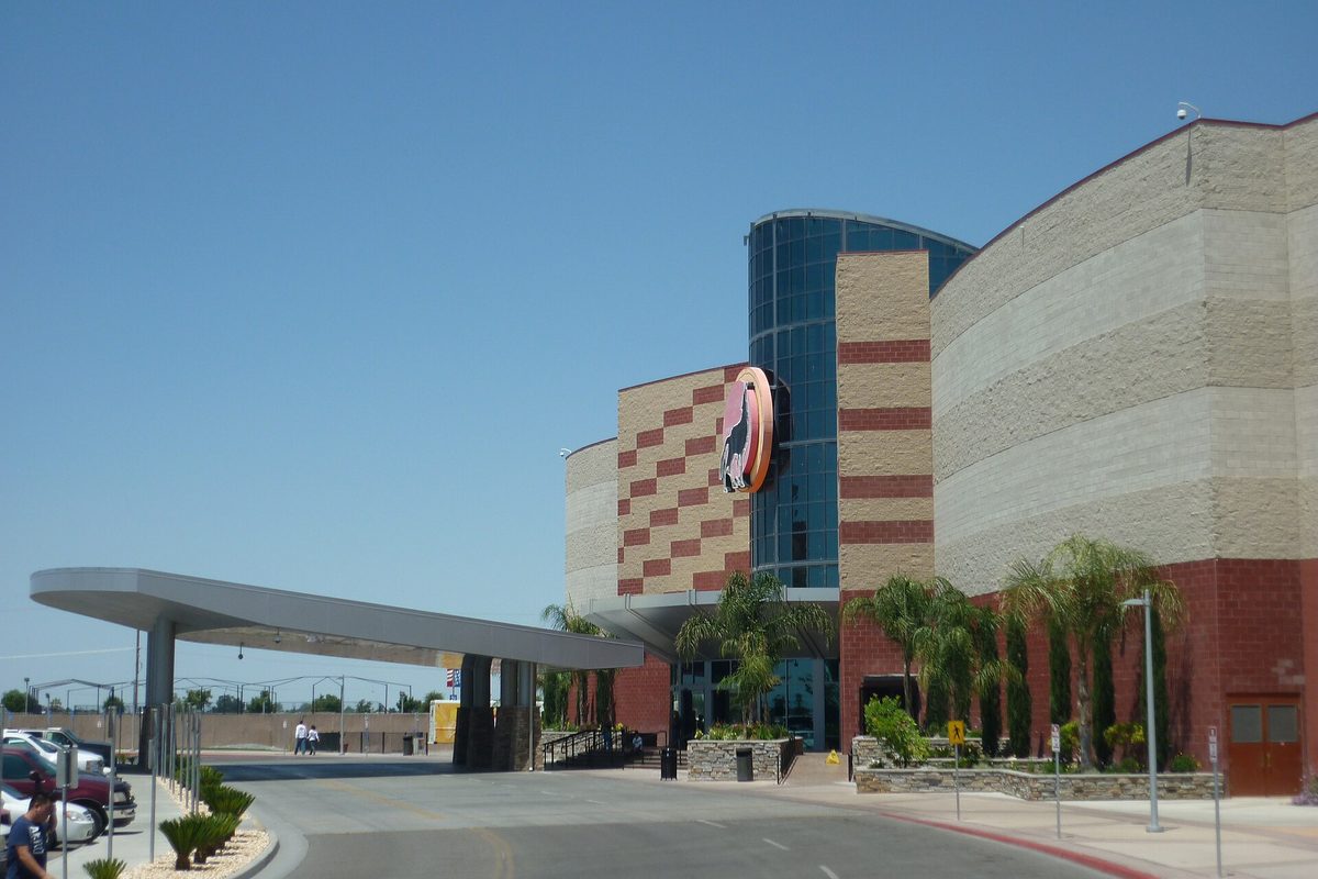 The entrance canopy and tiled tower of the Tachi Palace casino under a clear blue sky, with palm trees and parked cars