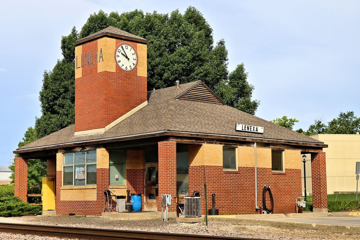 The red brick Lenexa depot with its clock tower and a Lenexa sign, beside the railroad tracks on a sunny day