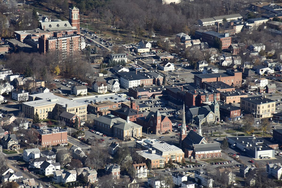 Aerial view of downtown Leominster: brick buildings, church steeples, parking lots and houses along tree-lined streets