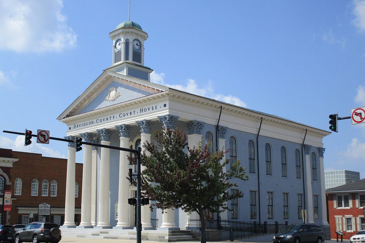 The white columned Old Davidson County Courthouse with a clock cupola, on the Square in Lexington under a blue sky, with traffic signals and parked cars