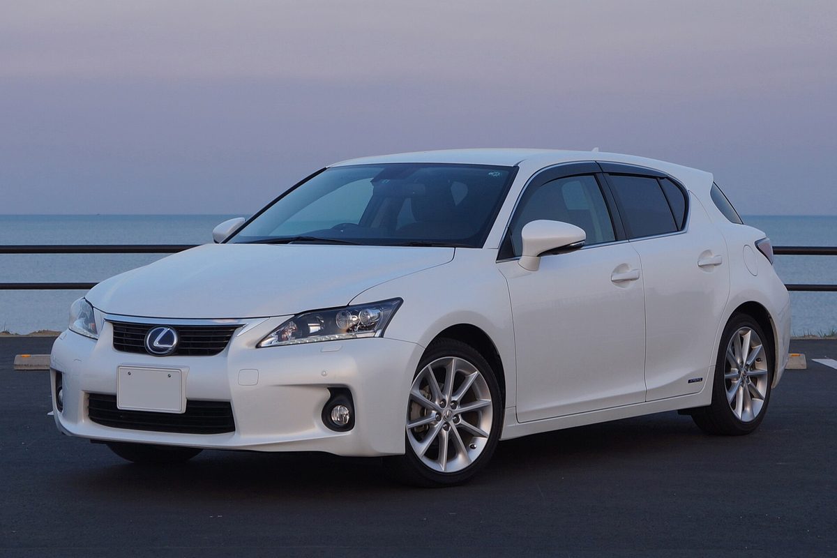 A white Lexus CT 200h five-door hatchback parked beside a seawall at dusk