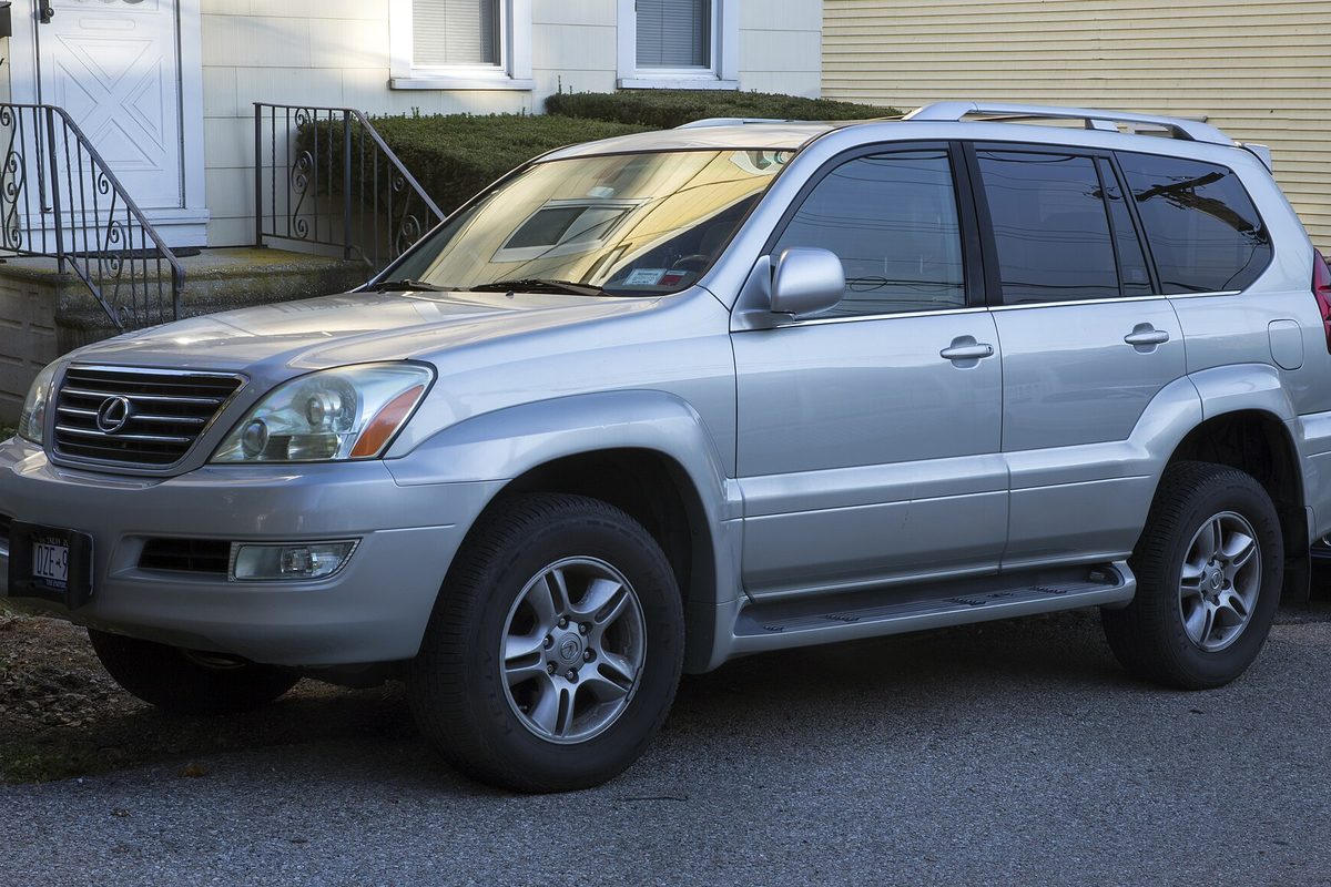 A silver first-generation Lexus GX 470 SUV with roof rails, parked on a driveway in front of a house