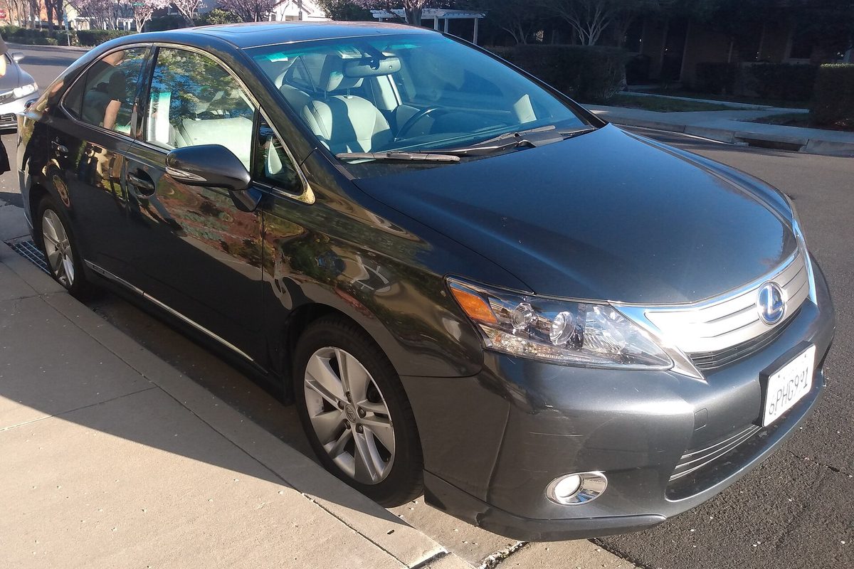 A dark gray Lexus HS 250h sedan parked at a curb on a sunny residential street