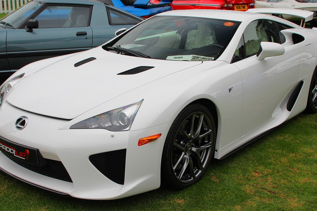 A white Lexus LFA two-seat coupe parked on grass at a car show, other classic cars behind it