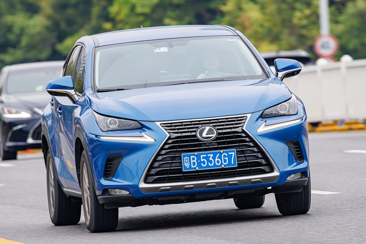 A blue Lexus NX compact SUV with a large spindle grille driving toward the camera on a city street