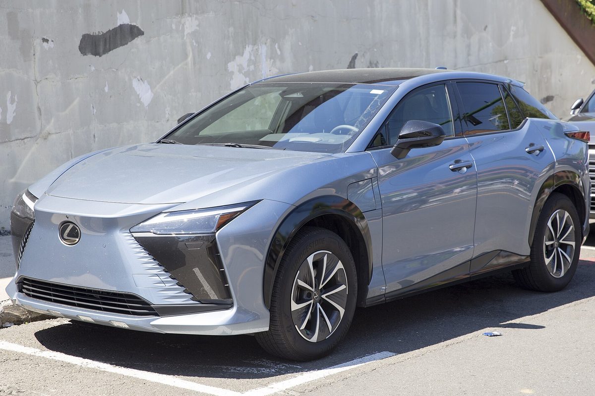 A silver-gray Lexus RZ 450e electric crossover parked in front of a stained concrete wall