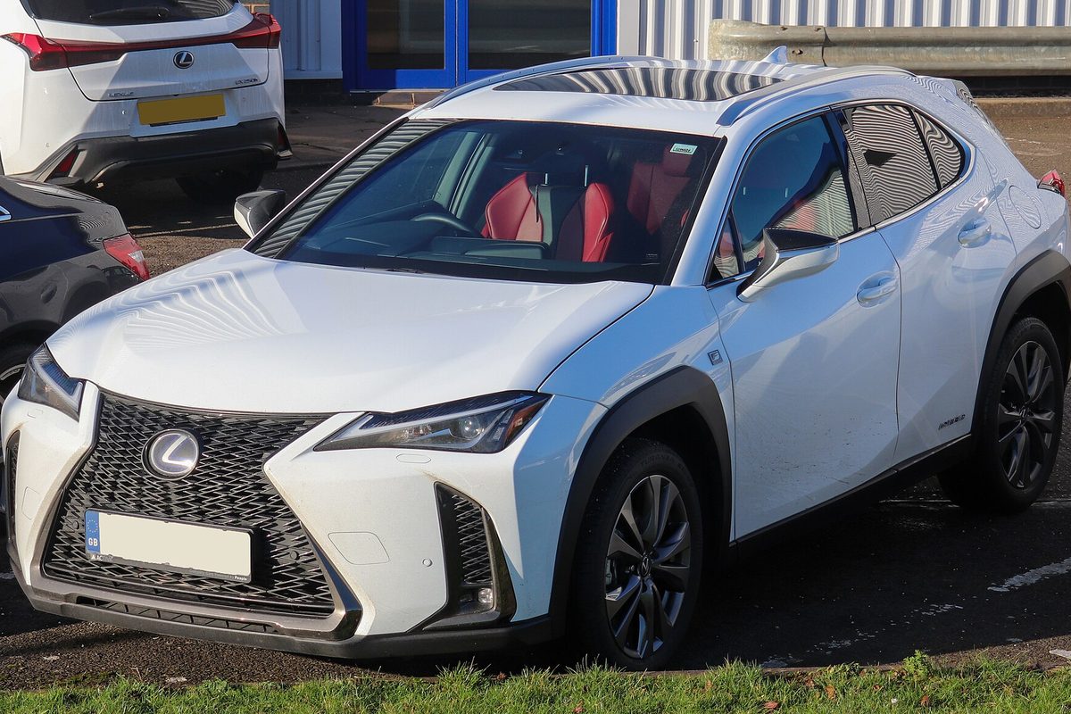 A white Lexus UX 250h F Sport crossover with red seats showing through the windshield, parked in a lot