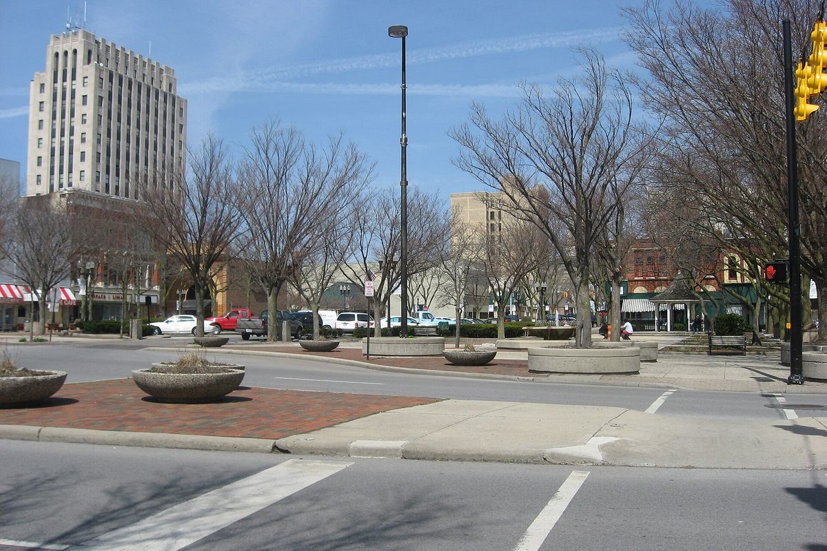 Lima's Public Square seen from its southeast corner, with bare trees, round concrete planters, a brick median and a tall pale office tower at the left