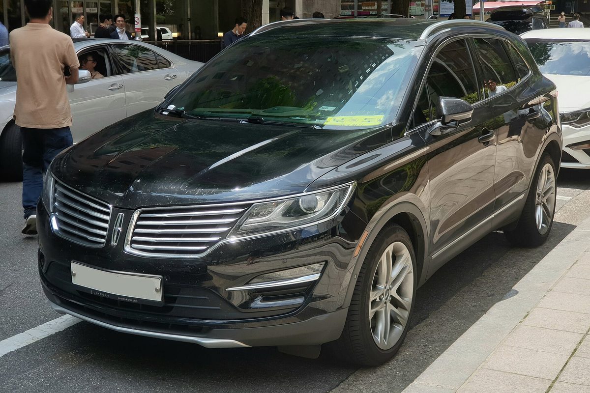 A black Lincoln MKC compact SUV parked at a city curb with people on the sidewalk behind it
