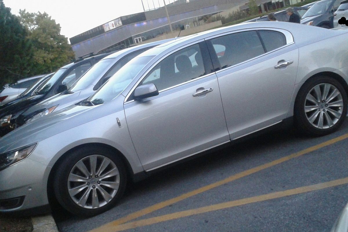 A silver Lincoln MKS sedan seen from the side, parked between yellow lines in a lot