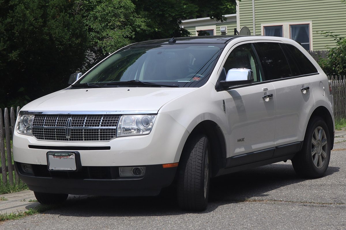A white 2009 Lincoln MKX crossover parked on a street in front of a pale green house and a wooden fence