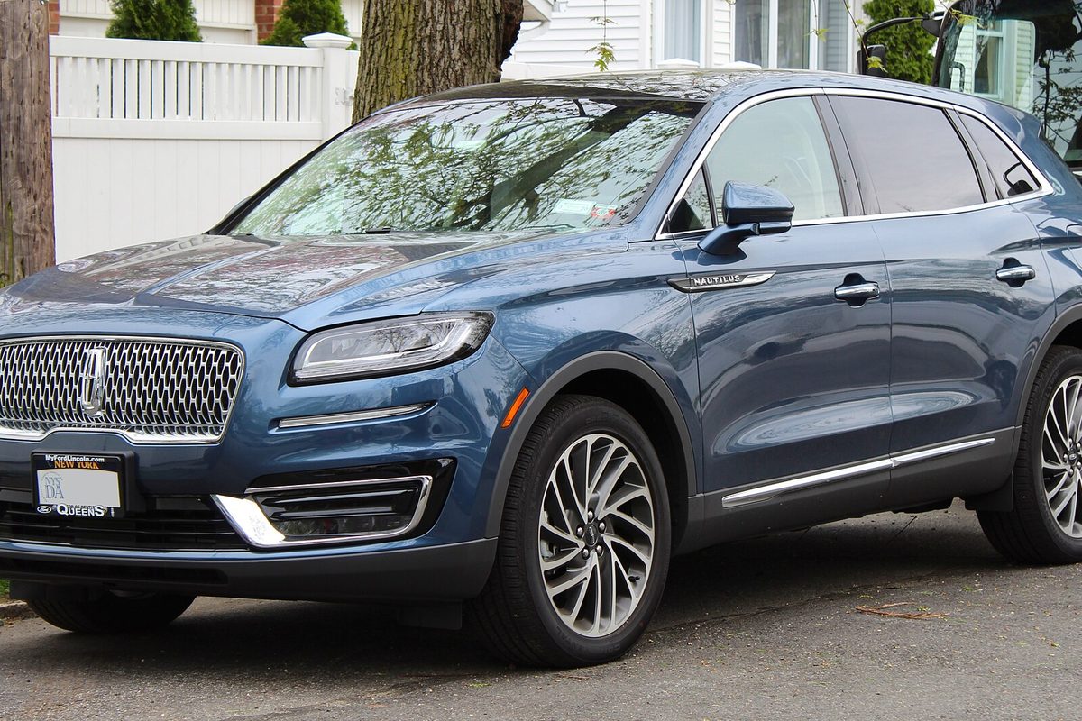 A blue Lincoln Nautilus SUV parked on a residential street in front of a white fence