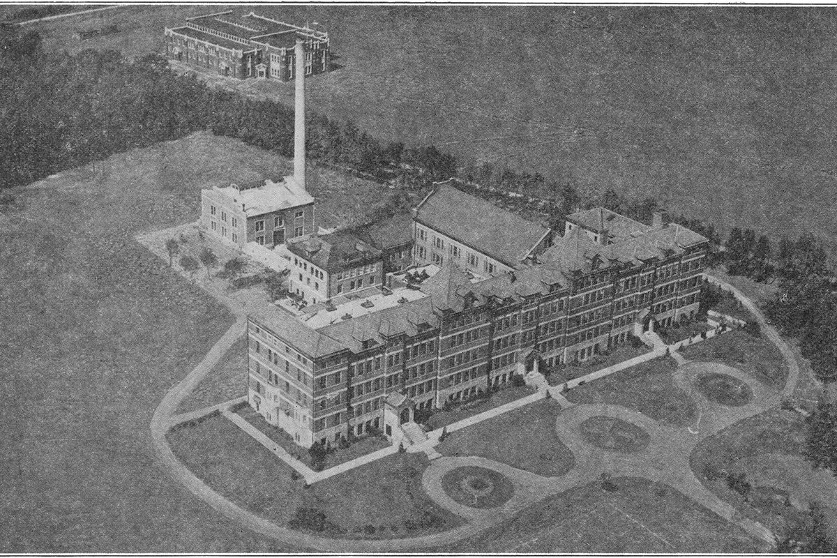 Old black-and-white aerial view of St. Procopius College in Lisle: a long multi-story brick hall, a tall smokestack and smaller buildings set among lawns and curving paths
