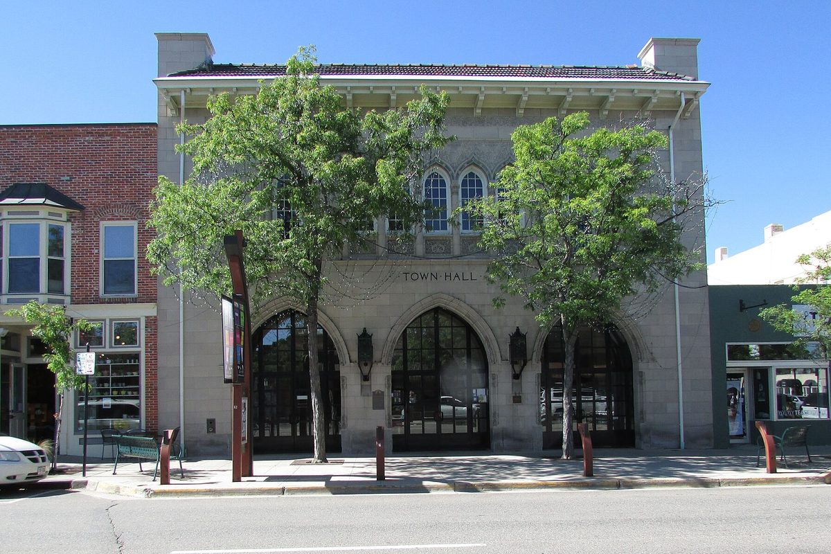 The pale stone Town Hall Arts Center on Main Street in Littleton, with three tall arched doorways and two leafy trees out front