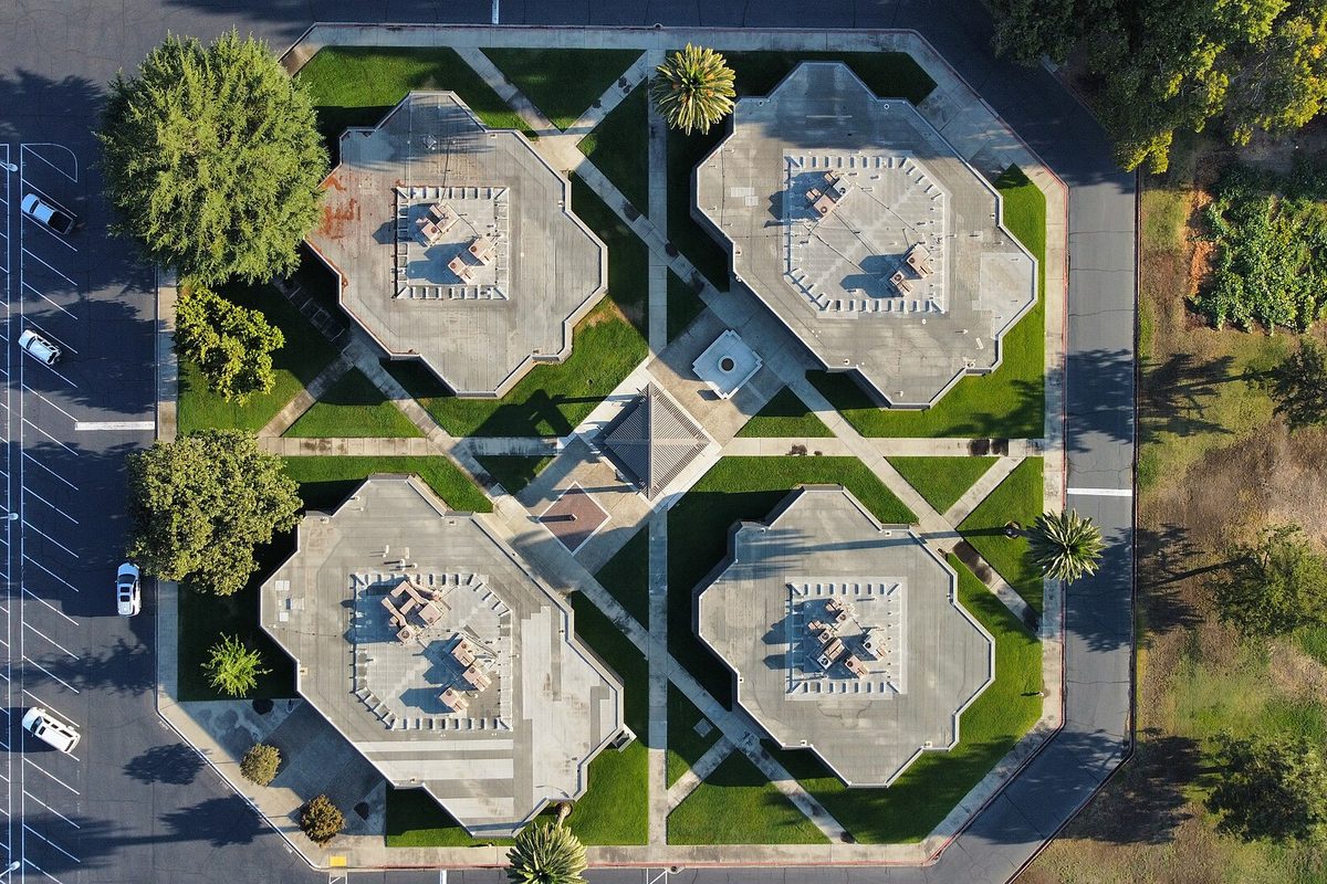 Drone view looking straight down on four octagonal flat-roofed buildings around a central court and pavilion at the Lodi Academy campus, beside a parking lot and trees