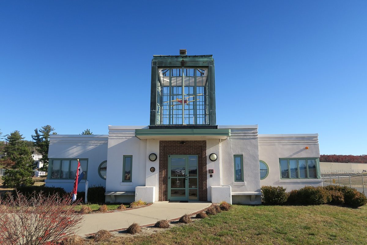 The Aviation Museum of New Hampshire, a white Art Deco building with round porthole windows and a tall green-framed glass tower over the door, under a clear blue sky