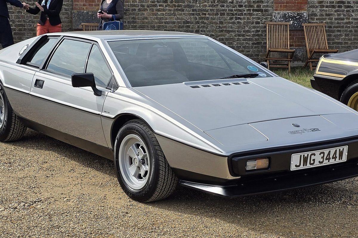 A silver and gray Lotus Esprit S2.2 wedge coupe with silver wheels, parked on gravel in front of a brick wall