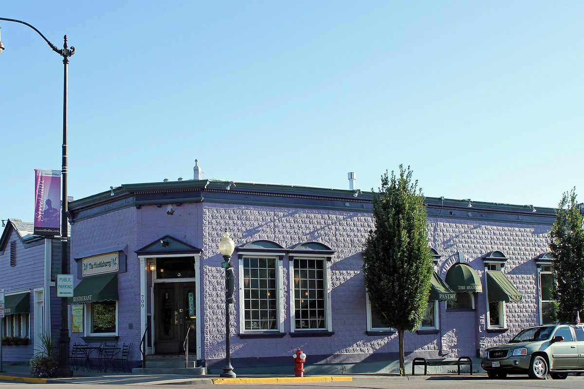 A lavender-painted historic brick building on a Main Street corner in Louisville, with green awnings, a street lamp and a parked SUV