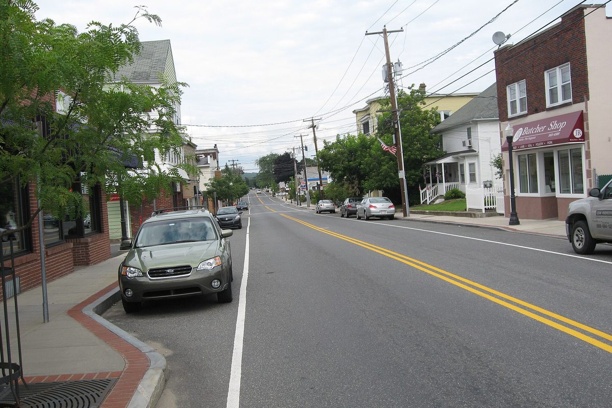 A downtown Ludlow street lined with brick storefronts, a butcher shop on the corner, parked cars along the curb and utility poles down the road