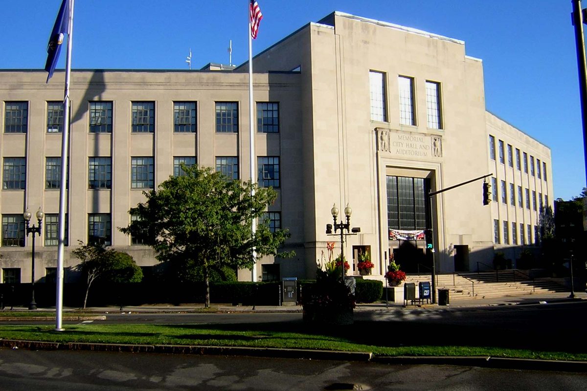 Lynn City Hall and Memorial Auditorium, a pale stone building with a tall central window bay, flags flying out front under a clear blue sky