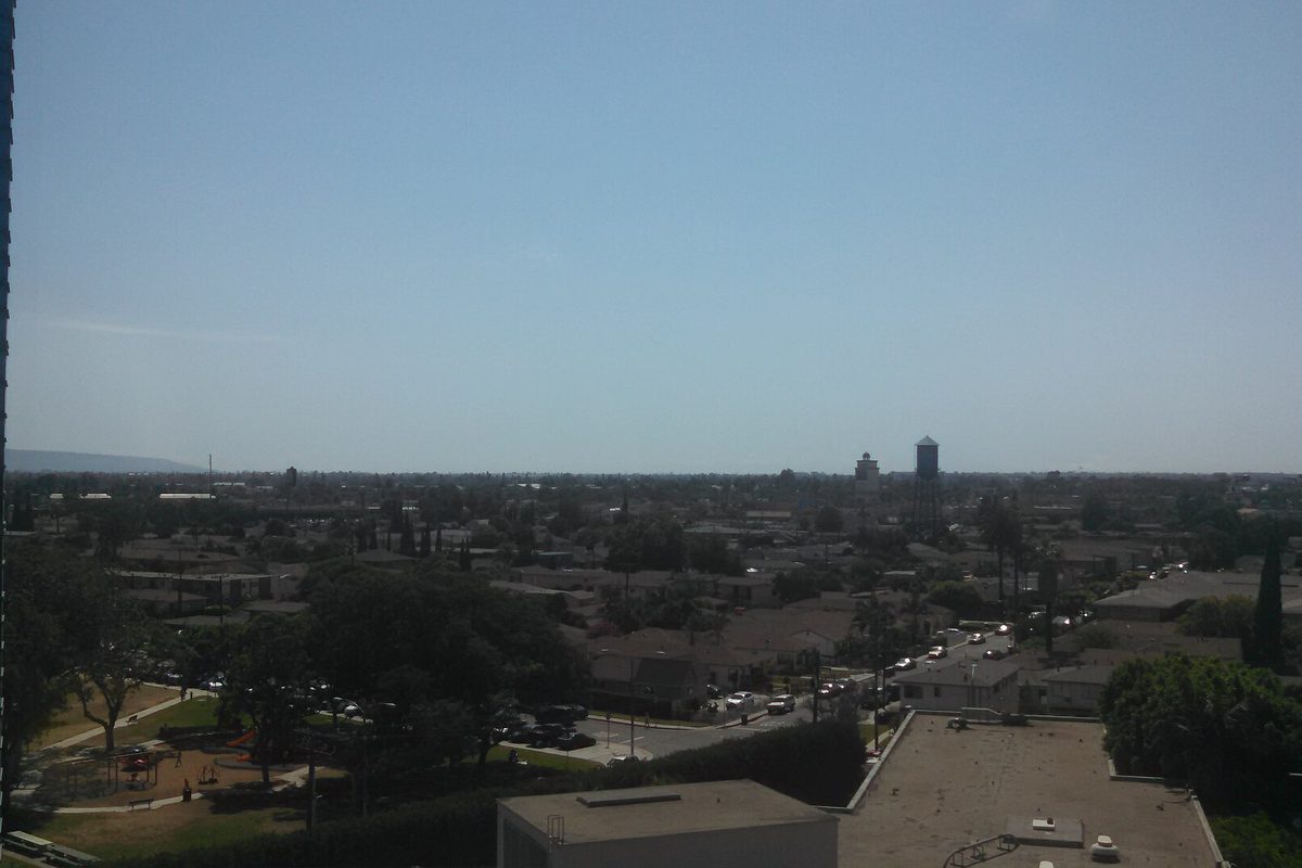 Flat rooftops, trees and a distant water tower across Lynwood under a hazy sky, seen from an upper floor of St Francis Hospital