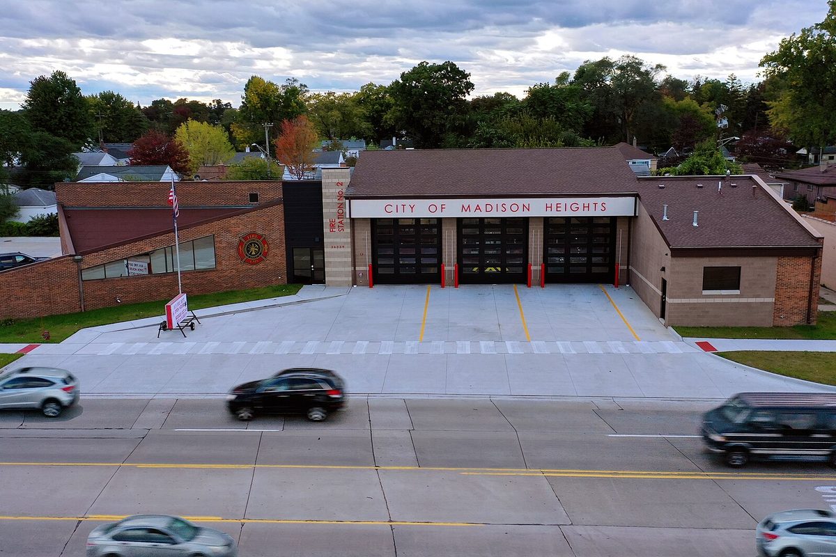 Madison Heights fire station seen from above, a brick building with three red-trimmed bay doors and a City of Madison Heights sign, with cars passing on the road in front