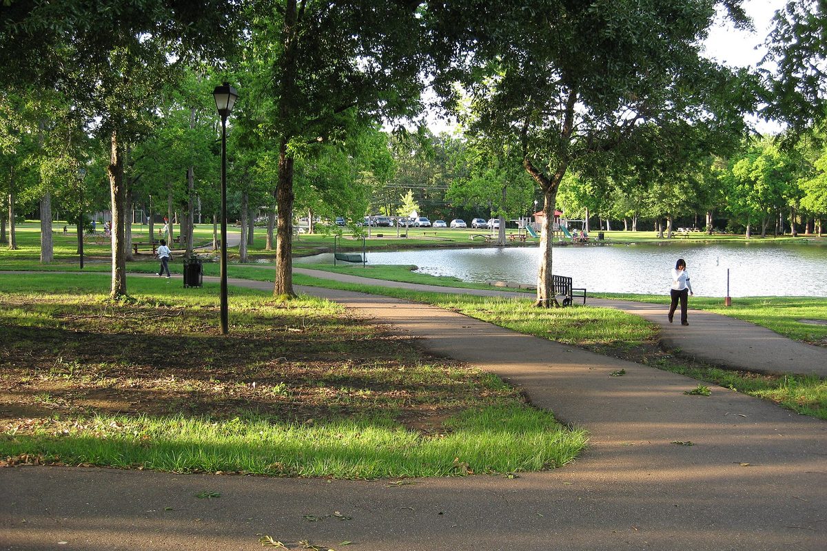 A paved walking path curving under shade trees beside the pond at Strawberry Patch Park in Madison