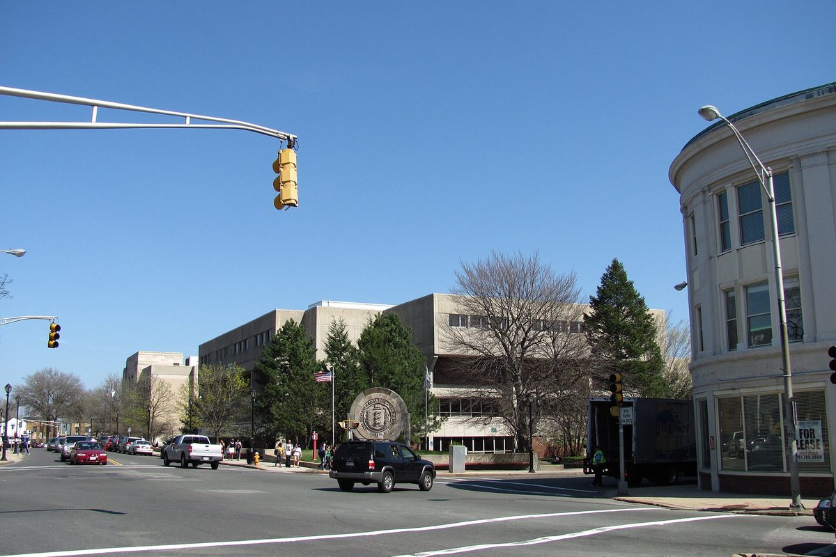 The intersection of Main, Salem and Ferry Streets in Malden, a traffic light overhead and the long Malden High School building behind it