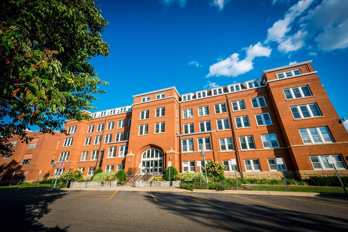 Red brick Old Main at Bethany Lutheran College in Mankato under a bright blue sky, with an empty parking lot in front