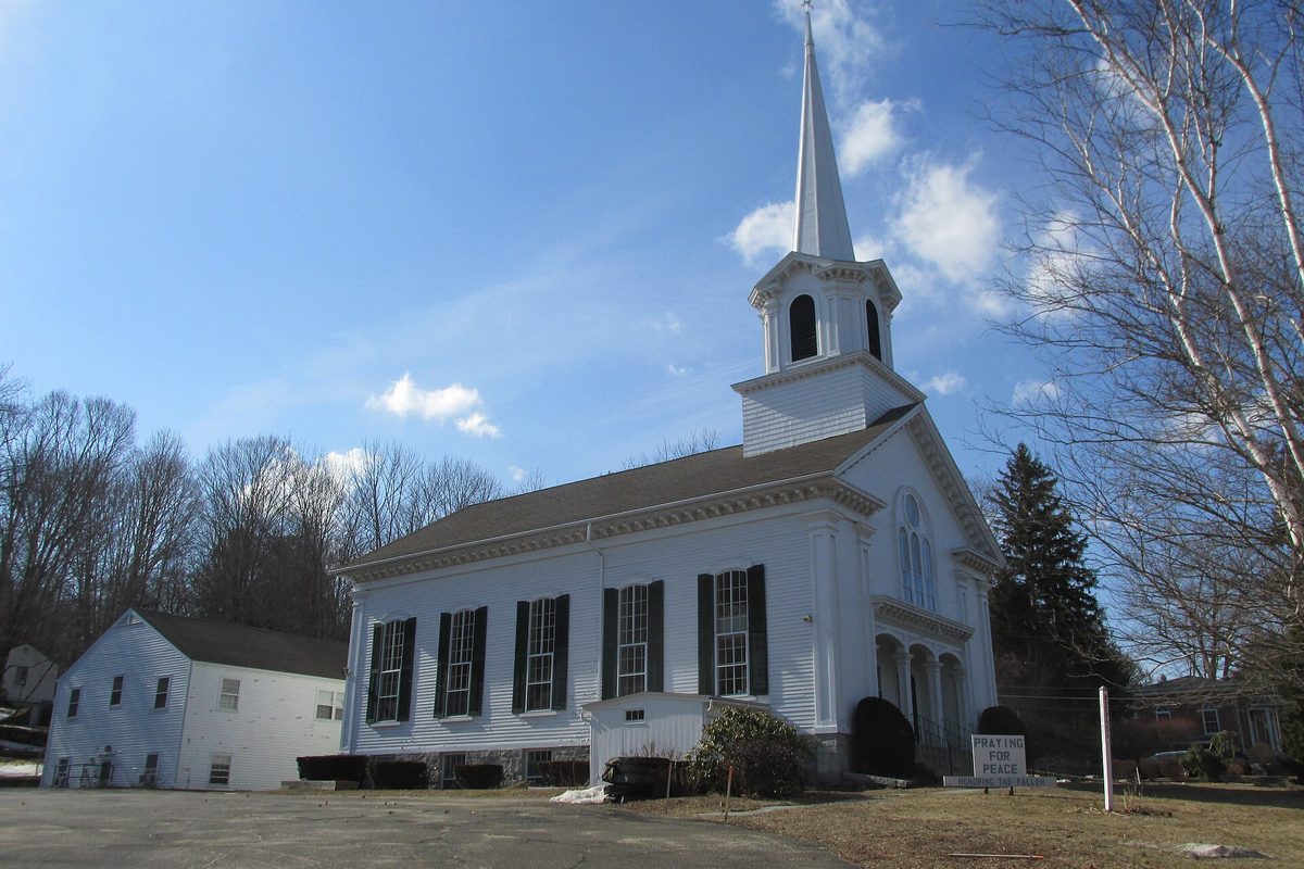 First Church of Christ in Mansfield, a white clapboard church with black shutters and a tall steeple, under a late-winter sky