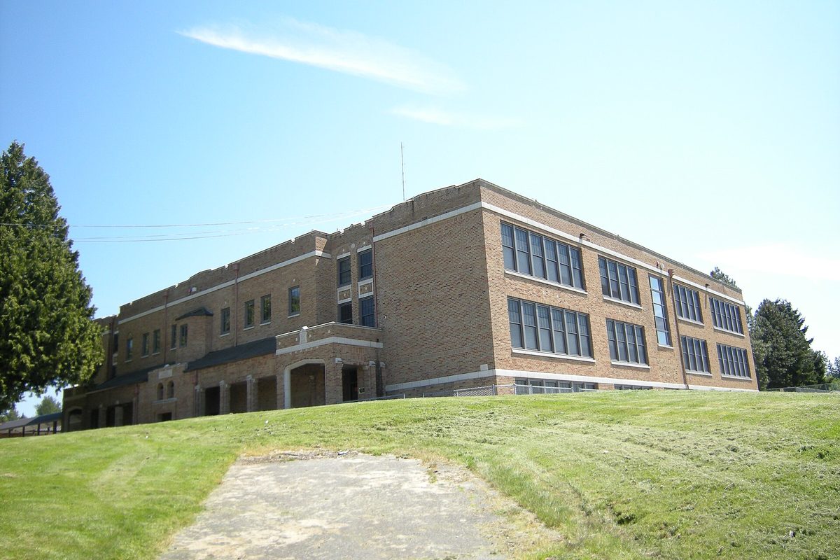 The tan brick Tahoma High School building in Maple Valley on a grassy rise, with evergreen trees and a blue sky