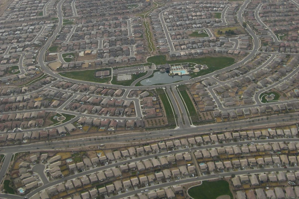 Aerial view of Maricopa's curving subdivision streets and rooftops around a green park with a pond and pool