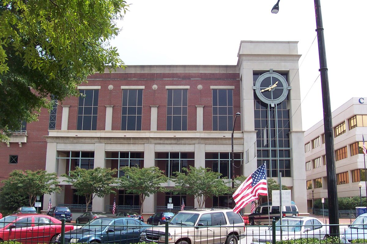 The Cobb County Courthouse in Marietta, a brick and stone building with a large clock on its corner tower, an American flag and cars parked in front