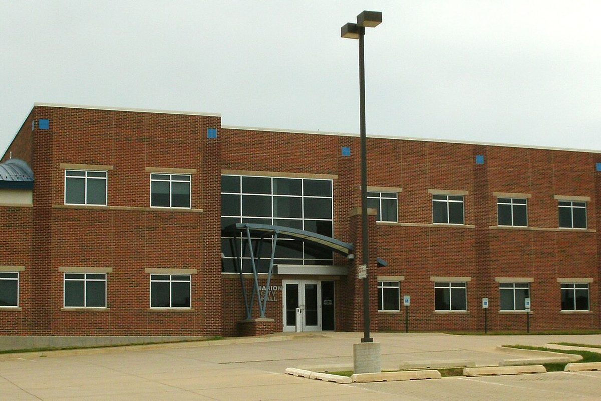 Marion City Hall, a two-story red brick building with a curved glass entrance canopy and a tall parking-lot light, under a grey sky