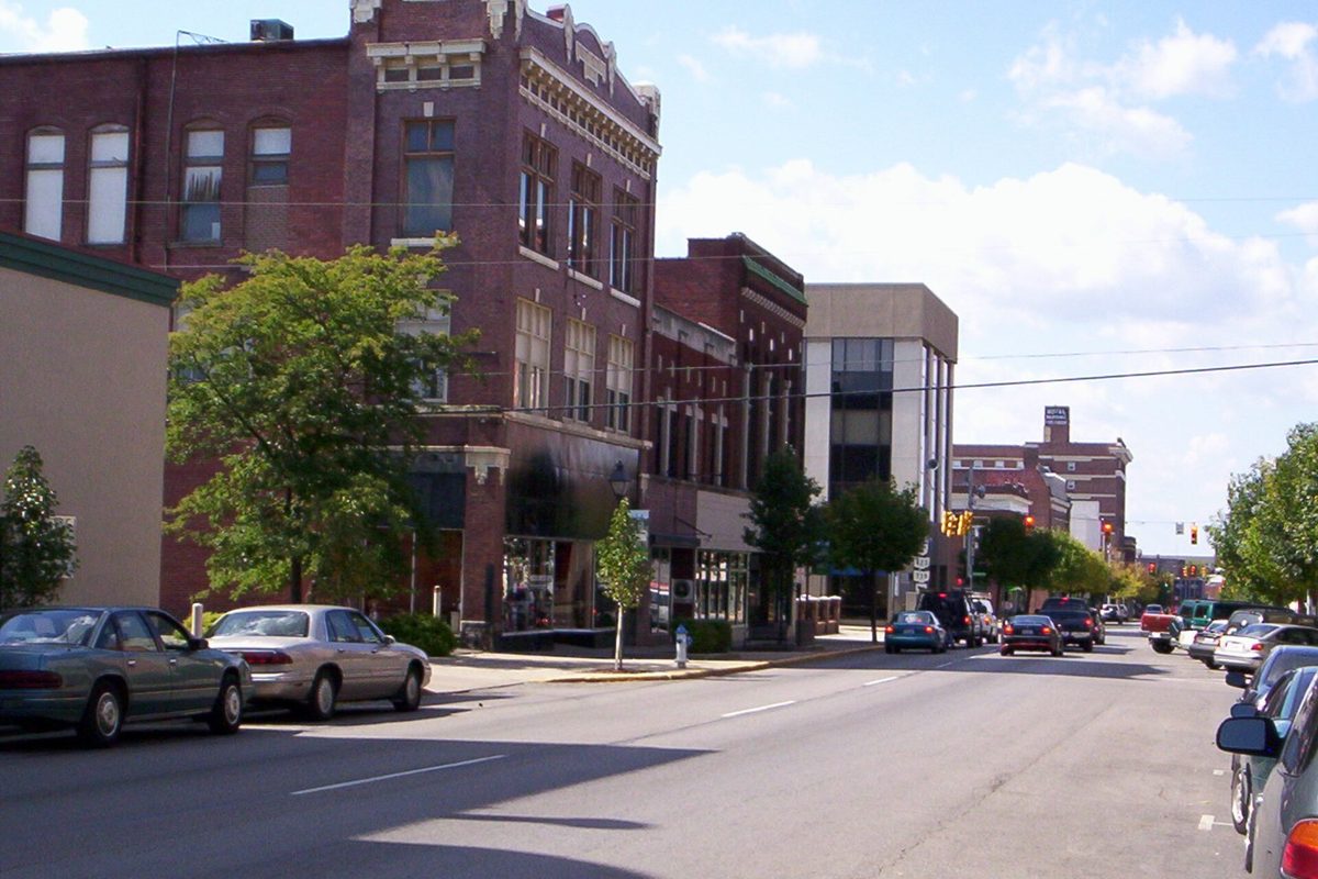 Red brick commercial buildings, street trees and parked cars along West Center Street in downtown Marion on a sunny day