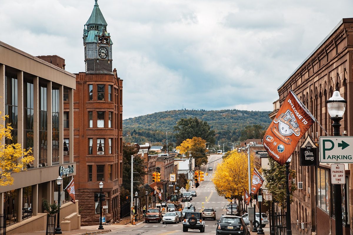 Downtown Marquette from North Front Street in autumn, a red stone clock tower on the left, yellow trees along the street and a wooded hill beyond
