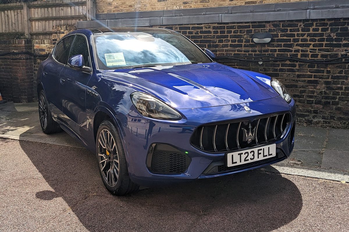 A blue Maserati Grecale SUV parked in a paved yard in front of a brick wall
