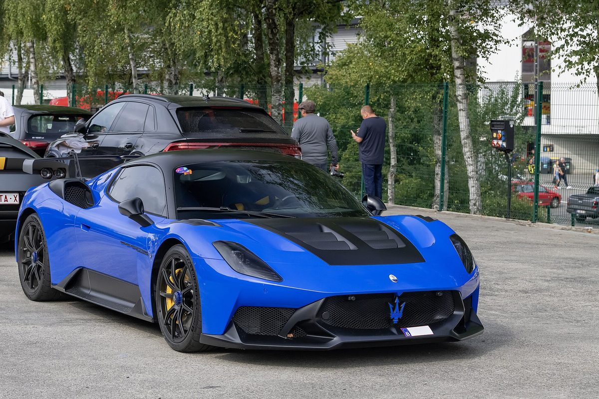 A bright blue Maserati GT2 Stradale with a black hood, black wheels and yellow brake calipers in a parking lot, people standing behind it
