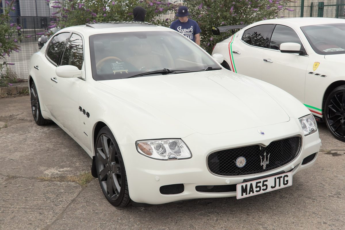 A white Maserati Quattroporte sedan with dark alloy wheels parked on gravel at an outdoor car show