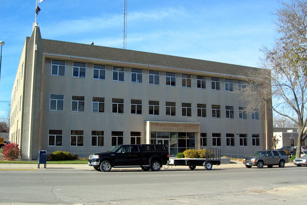 The pale, four-story Cerro Gordo County Courthouse in Mason City with a black pickup and flatbed trailer parked out front