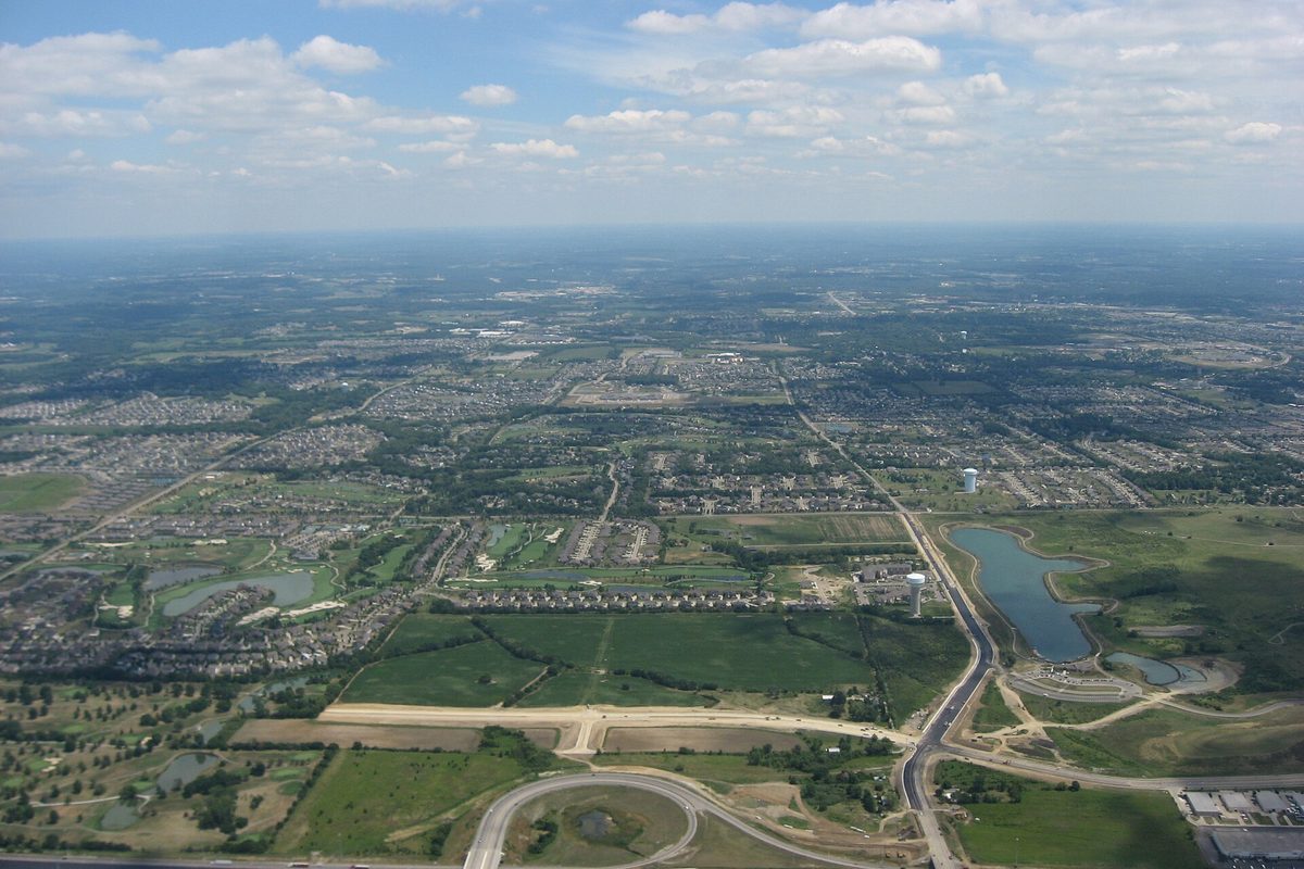 Aerial view of Mason from the west: housing subdivisions, green fields and a pond spread to the horizon, with Interstate 75 and an interchange in the foreground