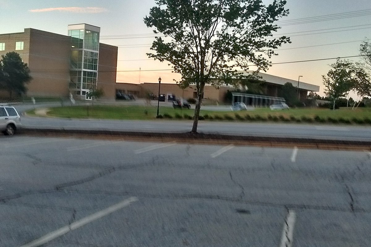 The side of Mauldin High School, a brick building with a glass stair tower, seen across a cracked parking lot at dusk