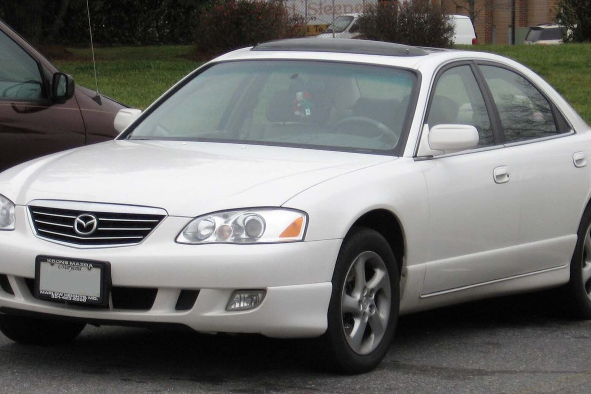 A white Mazda Millenia sedan with a sunroof, seen from the front corner in a parking lot