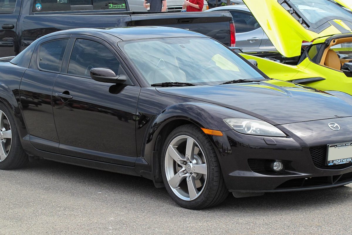 A black Mazda RX-8 coupe at a car show, seen from the front right, beside a yellow-green car with its hood up