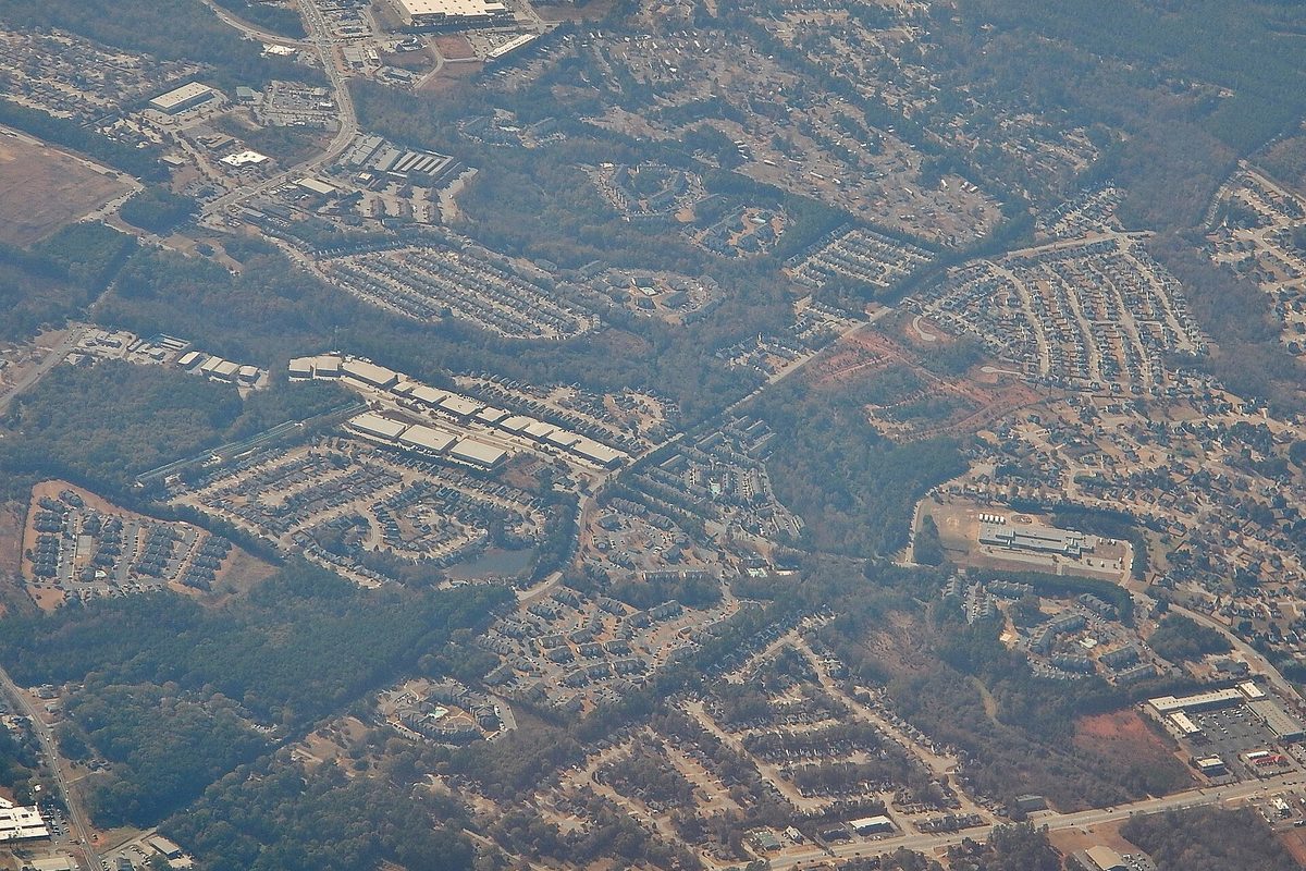 Aerial view from a plane over south metro Atlanta: subdivisions, apartment complexes and large warehouse roofs set among trees