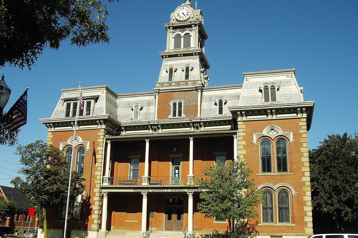 The Medina County Courthouse, a red brick building with a gray mansard roof and a white clock tower, against a clear blue sky
