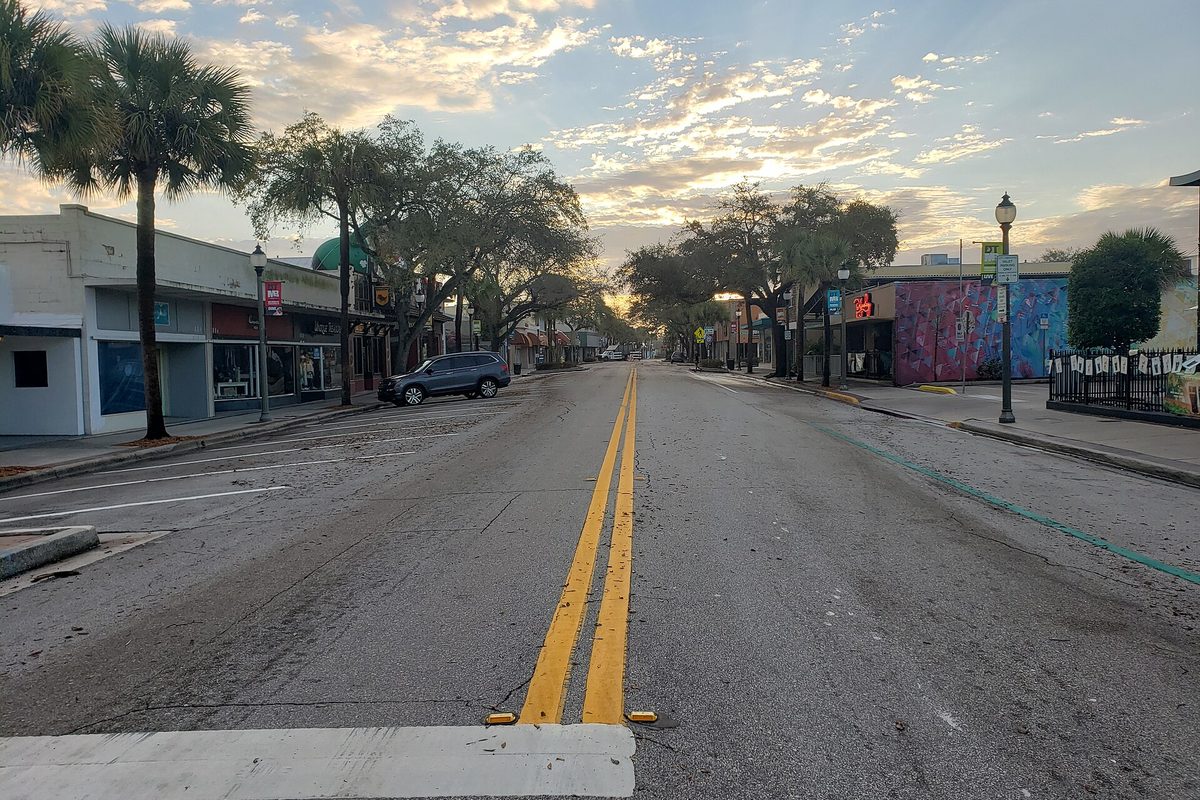 New Haven Avenue in downtown Melbourne at dawn, an empty street with double yellow lines, palm trees, storefronts and a painted mural wall