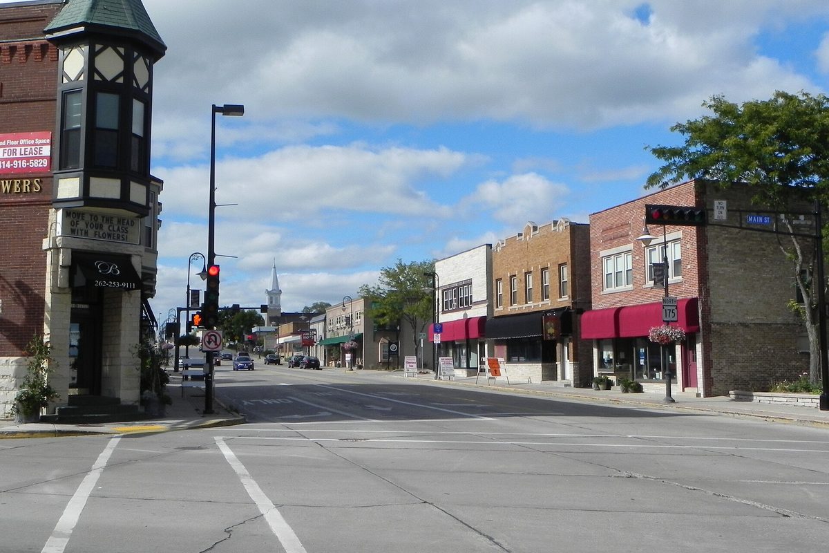 Main Street in the Menomonee Falls historic district, with brick storefronts, red awnings, a traffic signal and a white church steeple