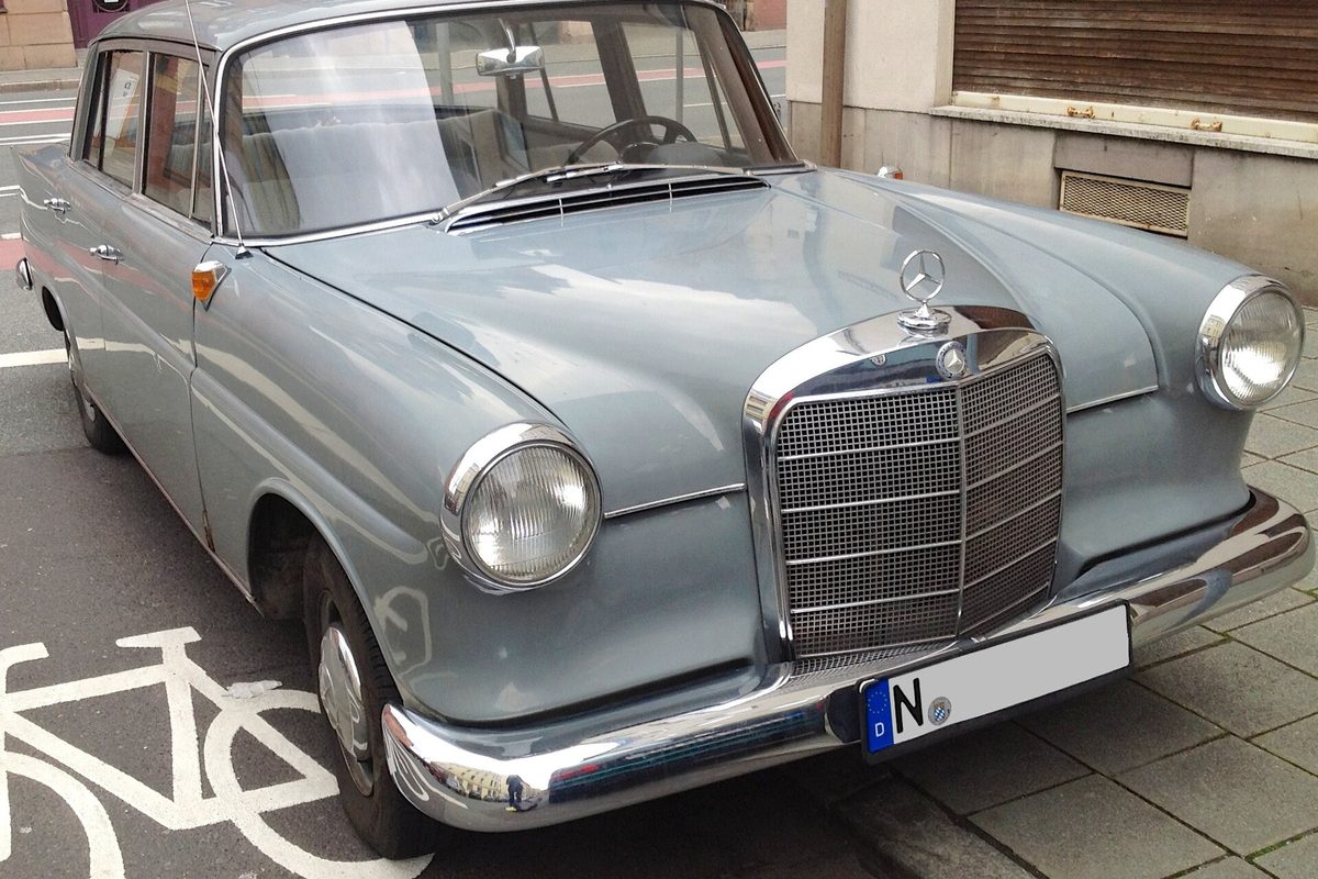 A light blue-gray early-1960s Mercedes-Benz 190 D fintail sedan parked at a curb beside a bike lane