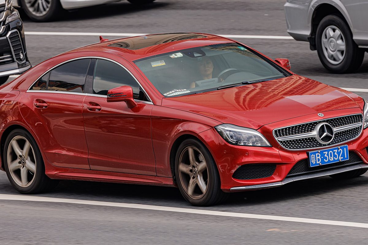 A red second-generation (C218) Mercedes-Benz CLS four-door coupe driving in city traffic
